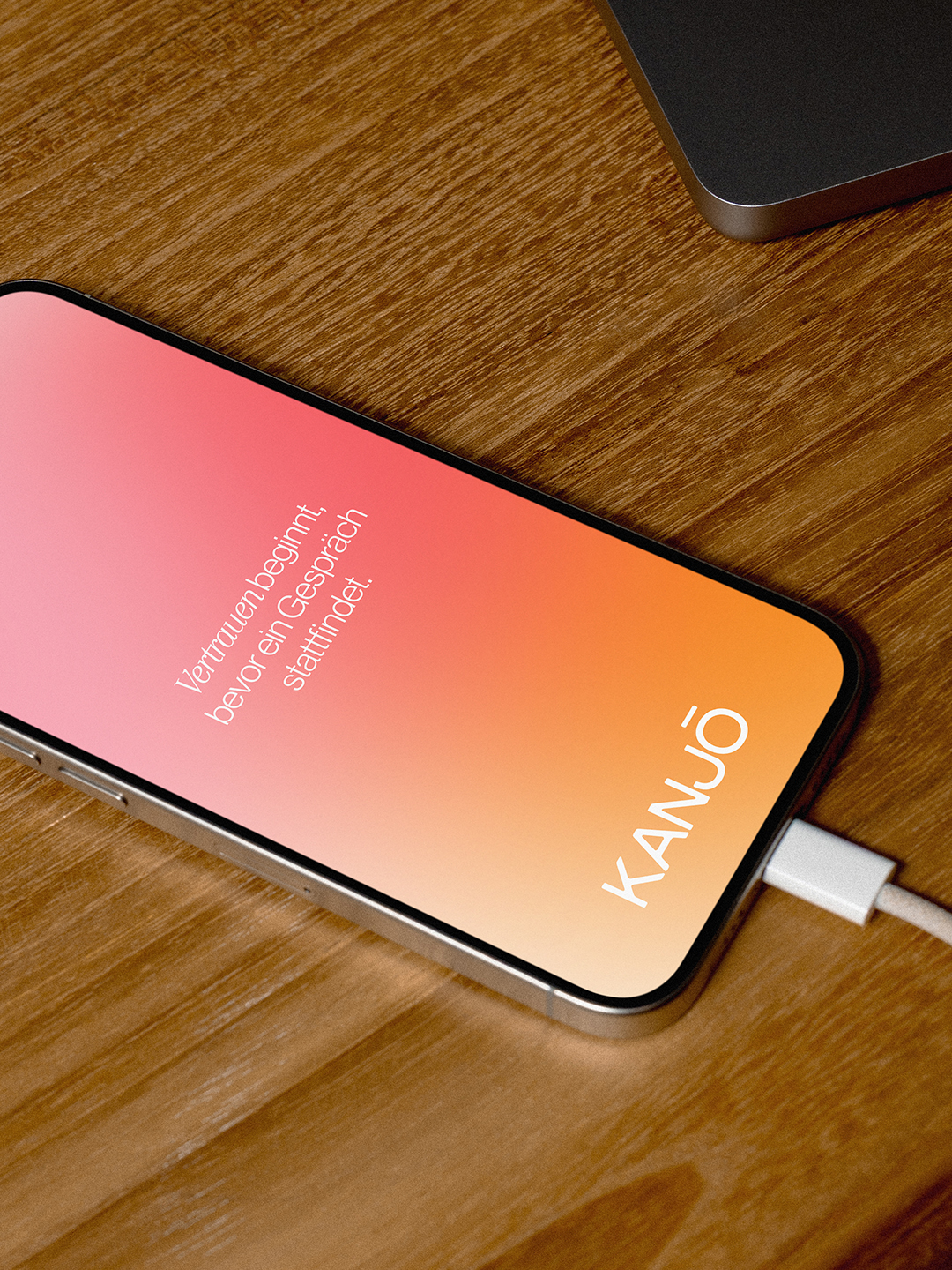 Smartphone mit Kanjō-Logo auf orangem Display am Ladekabel